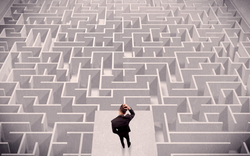 man standing on podium scratching his head while looking at a maze before him