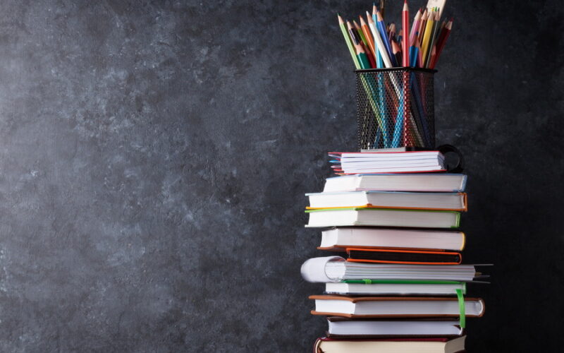 Books and supplies in front of classroom chalk board. Back to school concept with copy space