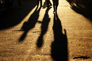 shadows on the ground of three people walking with yellow light behind them and the only thing you see of them is their shoes