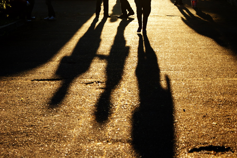 shadows on the ground of three people walking with yellow light behind them and the only thing you see of them is their shoes